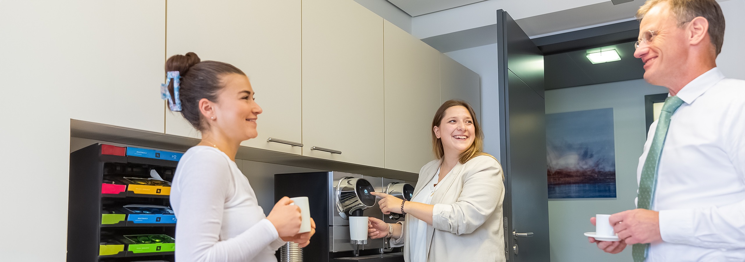 ws_karriere_image_01 In der Kaffeeküche des Notariats unterhalten sich drei Teammitglieder und lachen dabei